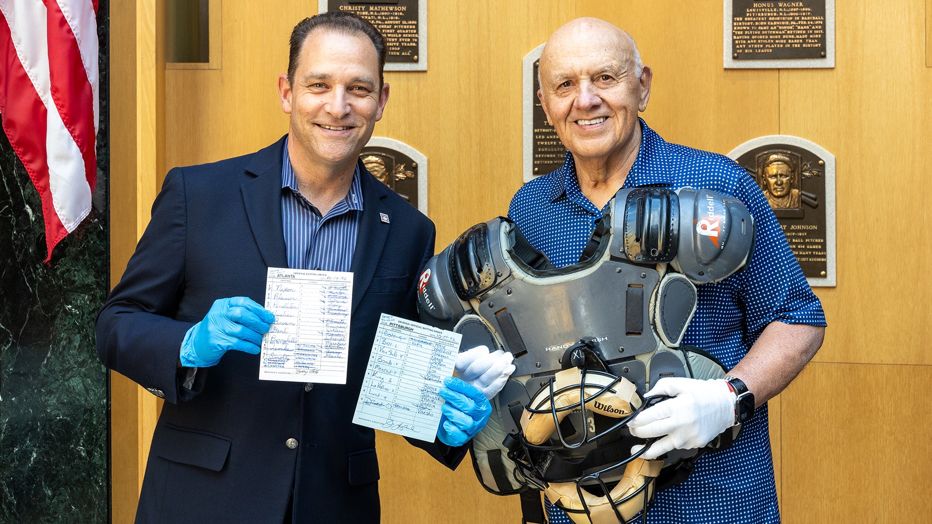Hall of Fame President Josh Rawitch and Randy Marsh hold lineup cards, mask and chest protector