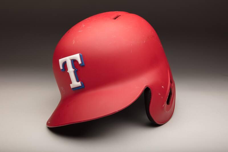 Red plastic batting helmet, size 7 1/4, with a proper left ear protector, a rubber white and blue "T" logo decal stuck on the front and an MLB logo and "29" stuck on the rear exterior.