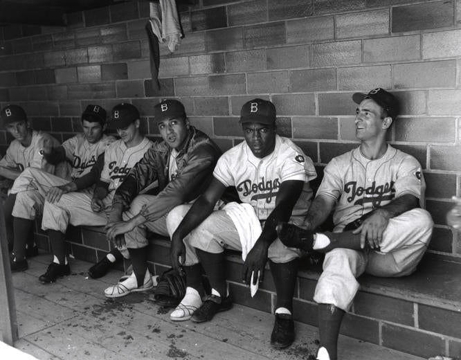 Six Brooklyn Dodgers sitting in the dugout at Doubleday.  From left to right: Phil Haugstad, Preacher Roe, Clem Labine, Don Newcombe, Jackie Robinson and Cal Abrams. (National Baseball Hall of Fame and Museum)