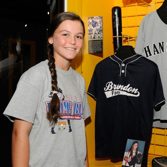 Chelsea Baker stands next to the jersey she donated to the Hall of Fame after pitching perfect game for her youth baseball team on April 9, 2010. (Milo Stewart, Jr. / National Baseball Hall of Fame)